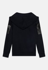 Felpa nera realizzata in tessuto morbido, con un ampio cappuccio, polsini a coste e eleganti toppe in pelle nera sulle spalle. Design minimalista.
