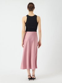 Débardeur noir à côtes associé à une jupe midi en satin rose, avec une texture lisse et un ourlet évasé, porté avec des sandales à talons noires.