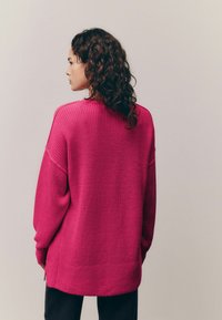 Pulover tricotat, cu croială lejeră, de culoare roz aprins. Are o textură ribbată, umeri căzuți și slituri laterale la tiv.