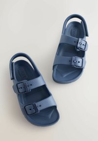 Sandale bleumarin din material sintetic texturat, cu două curele reglabile cu catarame și o buclă la călcâi pentru suport.