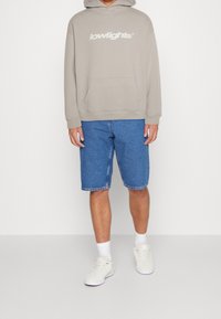 Felpa grigia chiara con logo "lowlights", tasca frontale; pantaloni corti in denim blu; calze bianche e sneakers; look casual e rilassato.
