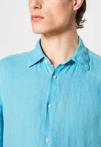 Heledad sinine särk, mis on valmistatud linast. Omab kraed, nähtavaid nööpe ja veidi kortsus tekstuuri, mis loob lõdva välimuse.