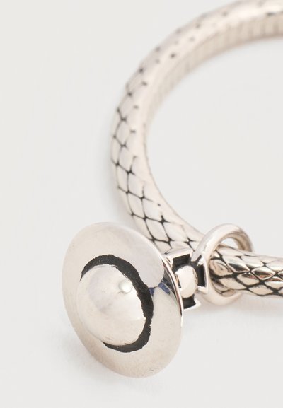 Ασημένιο πλεκτό βραχιόλι με στρογγυλό, θόλο σχήματος κούμπωμα που φέρει μαύρο σχέδιο σε σχήμα ημισελήνου σε ανοιχτό φόντο.
