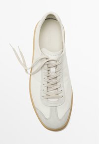 Weiße Sneaker aus Wildleder und Leder, mit runder Zehenform, flachen Schnürsenkeln und einer tanfarbenen Gummisohle. Glatte Oberflächenstruktur mit minimaler Gestaltung.