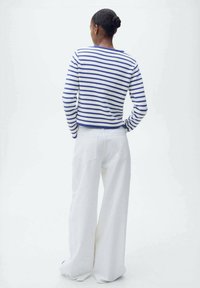 Maglione a maniche lunghe con righe blu e bianche; abbinato a pantaloni bianchi a gamba larga. Il maglione presenta una scollatura rotonda e polsini a coste.