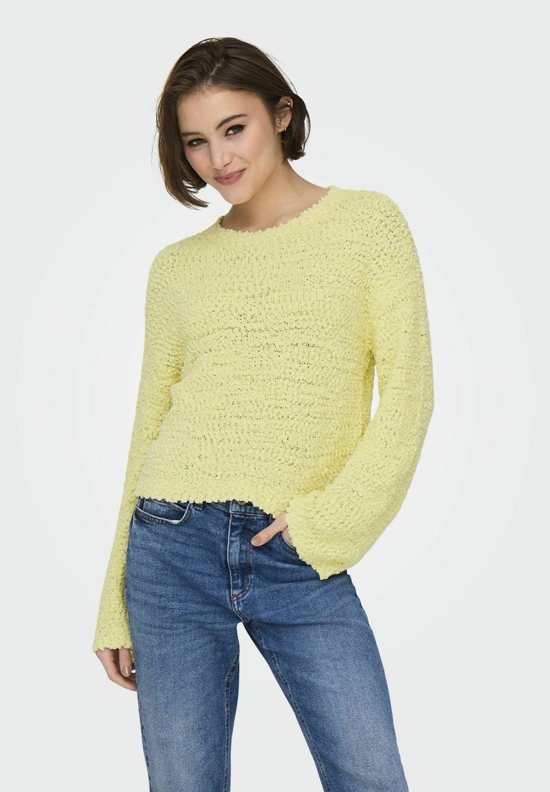 Maglione lavorato a maglia giallo limone con un motivo testurizzato, scollatura rotonda e maniche a campana; abbinato a jeans in denim blu.