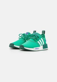 Zapatillas deportivas verdes con una textura suave, que cuentan con tres rayas blancas, acentos morados y una suela de goma texturizada.