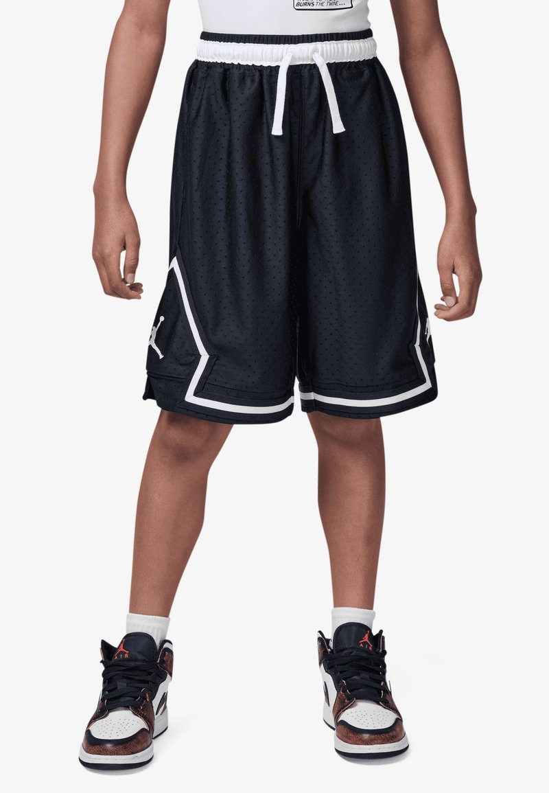 Zwarte mesh basketbalkorte broek met contrasterende witte rand en een logo, gecombineerd met bruin en witte hoge sneakers en witte sokken.