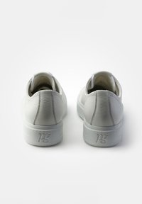 Baskets blanches en cuir avec une finition lisse, bout arrondi et col rembourré. Présente une lettrage en relief sur le talon et un design minimaliste.