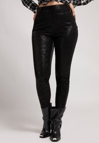 Leggings de cuero sintético negro con una textura lisa, cintura alta y corte ajustado, combinados con botas de tobillo negras con hebillas y acentos texturizados.