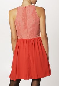 Bezramínková šaty s růžovým přiléhavým korzetem a splývavou červenou sukní, vyrobené z hladkého materiálu. Obsahuje zip na zadní straně.