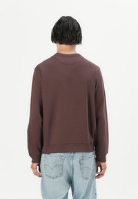 Brun crewneck genser med ribbestrikkede mansjetter og nederkant, paret med lyseblå avslappede jeans. Glatt tekstur, minimal design.