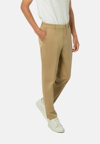 Khaki-Hosen mit Slim-Fit, aus glattem Stoff gefertigt. Verfügt über schräge Taschen und eine flache Vorderseite, kombiniert mit weißen Sneakern.