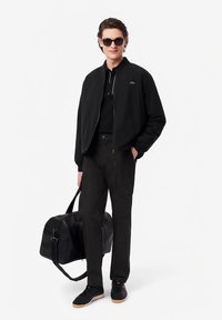 Μαύρο μπουφάν bomber, μαύρο πόλο, μαύρο παντελόνι cargo και μαύρα αθλητικά παπούτσια. Τα αξεσουάρ περιλαμβάνουν γυαλιά ηλίου και μια μαύρη τσάντα duffel.