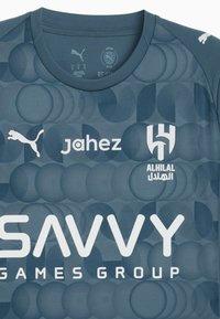 Jersey deportivo gris con un patrón texturizado de círculos superpuestos. Presenta logotipos en blanco de PUMA, Jahez y SAVVY Games Group.