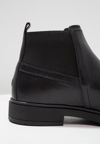 Mustat nahkaiset nilkkurit, joissa on joustavat sivupaneelit ja kumipohja. Ominaisuuksiin kuuluu sileä pinta ja hienovarainen ompelu saumoissa.