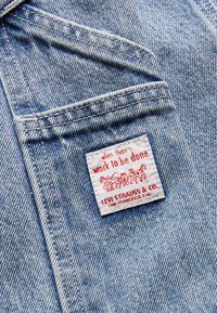 Tela de mezclilla de color azul claro con una etiqueta blanca que tiene texto y un gráfico en rojo. La etiqueta dice "cuando hay trabajo que hacer" con detalles de marca.