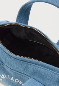 Saco de denim azul com fecho com zíper, apresentando um forro interior preto e um logótipo no exterior. Alças curtas e textura suave.