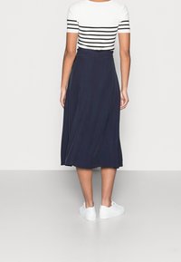 Navy A-line skirt with a flowing design, paired with a white and black striped top. Footwear consists of white sneakers.