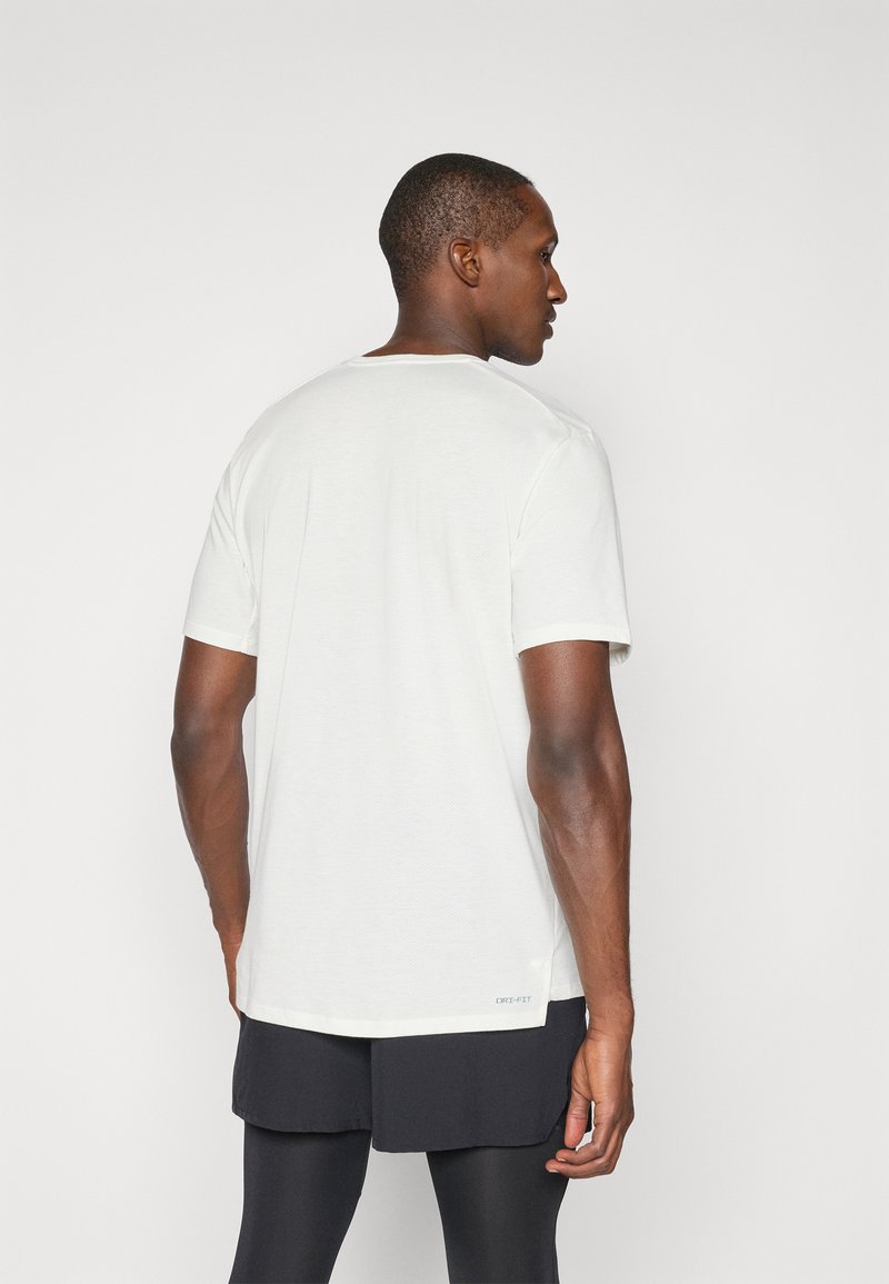 Biała koszulka z krótkim rękawem z okrągłym dekoltem i teksturowaną powierzchnią. Widoczna metka "DRI-FIT" na dole. Noszona z czarnymi szortami.