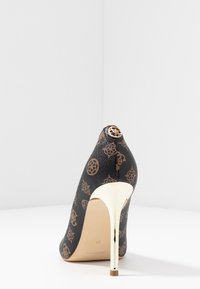 Chaussure à talons hauts avec une tige en cuir texturé noir présentant des motifs de logo marron, un talon aiguille doré et un accent décoratif doré à l'arrière.