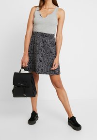 Šedý žebrovaný top bez rukávů s výstřihem do V, spárovaný s sukní s hadím potiskem v černé a šedé barvě. Celkový vzhled doplňuje černý batoh a černé tenisky.