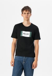 Svart bomull t-skjorte med et hvitt og grønt rektangulært grafikk med "JACK & JONES" i sentrum. Korte ermer og rund hals.