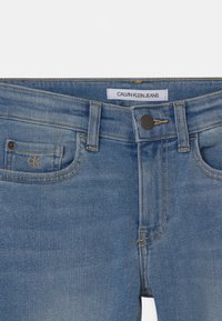 Světle modré džíny z denimu s klasickým pětikapsovým designem, zapínáním na knoflík a značkovou etiketou. Jemné švy na látce.