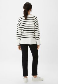 Gestreepte zwart-witte sweater met een losse fit, van achteren gezien. Gecombineerd met zwarte broek en witte sneakers. Soepele textuur, geribbelde zoom.