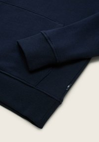 Granatowa bluza z dzianiny z prążkowanymi ściągaczami przy mankietach i dole. Wykonana z teksturowanego materiału, z boczną metką z logo. Klasyczny fason typu pulower.