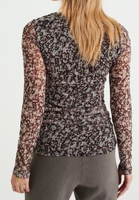 Långärmad topp i genomskinligt, åtsittande tyg med ett flerfärgat stänk-mönster av brunt, grönt och rosa. Rynkdetaljer vid midjan.