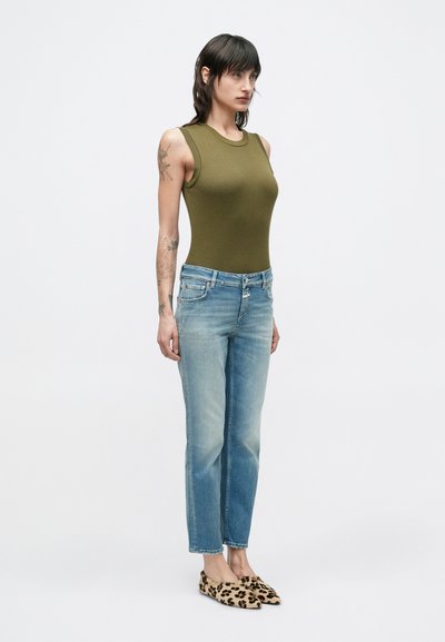 Body sans manches vert olive au design ajusté, associé à un jean droit bleu clair. Des ballerines à imprimé léopard remarquables complètent le look.