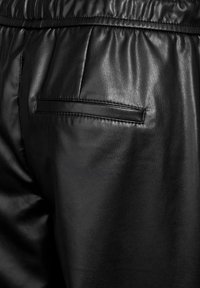 Zwarte leren broek met een gladde textuur, elastische tailleband en een paspelzak aan de achterkant. Close-up van de stiksels en het materiaal.