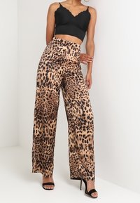 Leopardmönstrade vida byxor med en slät yta, ljusbrun bas och mörka fläckar; kompletterat med en svart crop top och högklackade skor.