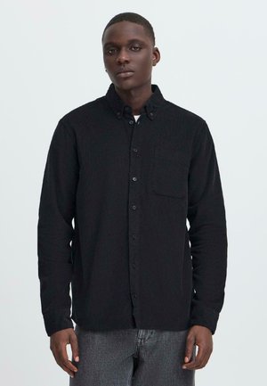 Black button-up shirt in textured fabric, featuring a pointed collar, front pocket, and long sleeves, worn over gray pants.