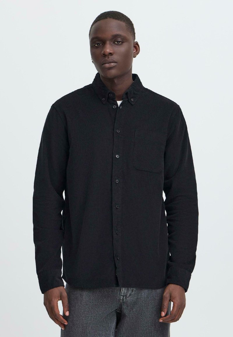 Black button-up shirt in textured fabric, featuring a pointed collar, front pocket, and long sleeves, worn over gray pants.