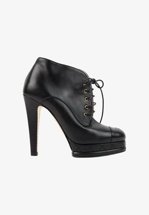 Bottine noire en cuir à talon haut, devant à lacets, œillets dorés, bout renforcé cousu et semelle plateforme matelassée.
