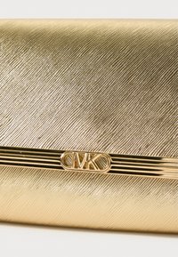 Χρυσή υφασμάτινη τσάντα με μορφή κλειδώματος και διαγώνιο σχέδιο, που διαθέτει μεταλλικό λογότυπο και κομψό, ορθογώνιο σχήμα.