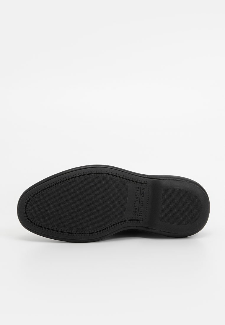 Semelle de chaussure en caoutchouc noir avec une surface texturée, une forme contournée et des détails de couture le long du bord. Comprend le marquage de la marque sur le lit de pied.