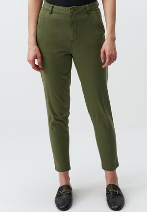 Pantaloni verde oliva slim fit, con chiusura a bottone, tasche frontali e una texture liscia. Abbinati a mocassini neri.