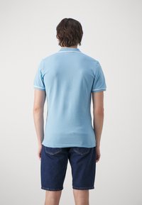 Jasnoniebieska koszulka polo z klasycznym kołnierzykiem i białymi akcentami, połączona z ciemnymi dżinsowymi szortami. Tkanina wydaje się gładka i przepuszczająca powietrze.