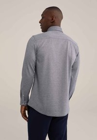 Camisa gris de manga larga con un patrón texturizado, puños abotonados y un cuello afilado, vista desde la espalda sobre un fondo neutro.