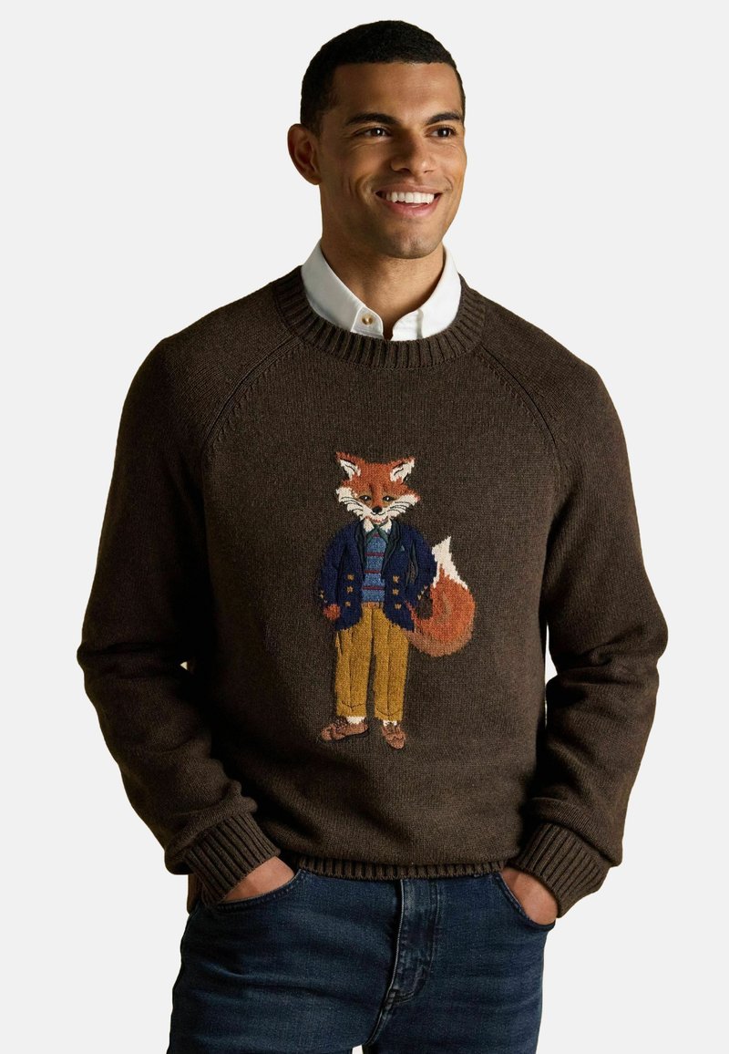 Brauner Strickpullover mit einem gestickten Fuchs in blauer Jacke und gestreiftem Hemd, mit gerippten Bündchen und Saum, über blauen Jeans getragen.