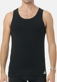 Svart atletisk linne gjort av ett slätt tyg. Har rund halsringning och breda ärmhål. En liten vit logo är placerad längst ner till höger.