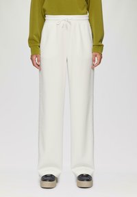 Białe dresowe spodnie w luźnym kroju z elastycznym pasem, z bocznymi szwami o kontrastowej fakturze, w zestawieniu z czarnymi butami na platformie.