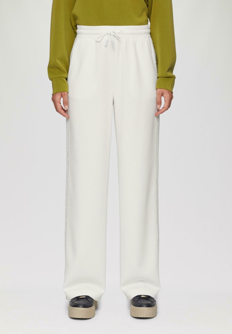 Białe dresowe spodnie w luźnym kroju z elastycznym pasem, z bocznymi szwami o kontrastowej fakturze, w zestawieniu z czarnymi butami na platformie.