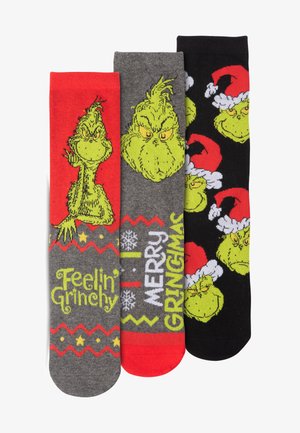 Tre paia di calzini con il Grinch. Colori: rosso, grigio, nero. I design includono facce del Grinch e frasi festive in caratteri bold.
