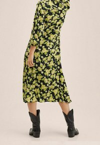 Robe florale avec des motifs verts et blancs sur un fond noir, dotée de manches trois-quarts et d'une silhouette fluide, accompagnée de bottes noires.