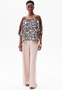 Zwart-wit gestreepte top met oranje accenten, losse pasvorm, brede mouwen; gecombineerd met lichtbeige wijde broekspijpen. Gladde stof, casual stijl.