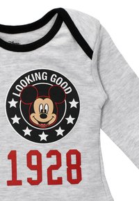 Grau gefütterter Einteiler mit schwarzen Akzenten. Enthält ein kreisförmiges Mickey-Maus-Graphic, "LOOKING GOOD" und das Jahr "1928" in fettem roten Text. Weicher Stoff.